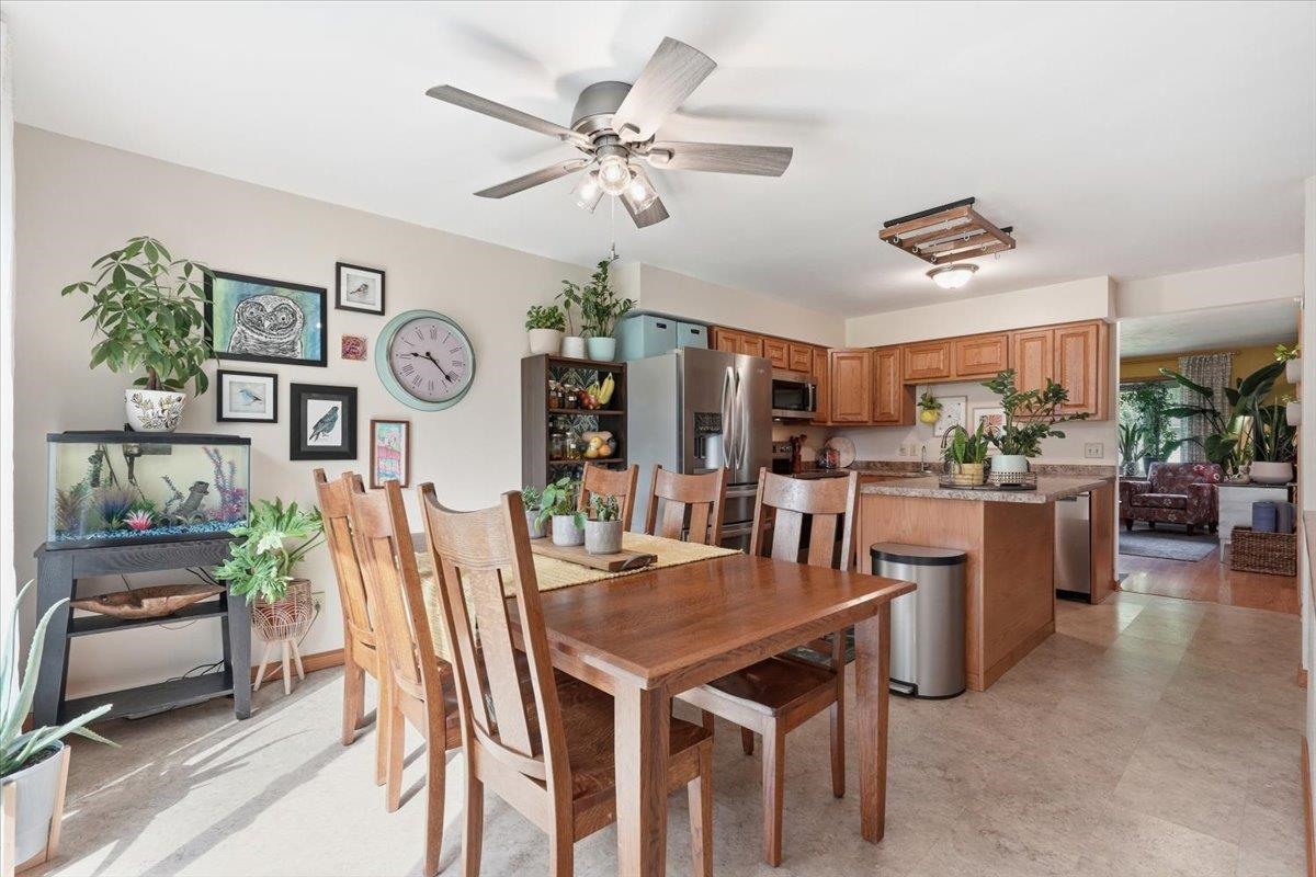 Dining area with a large wooden table, opening to a kitchen with wood cabinets and stainless steel appliances.