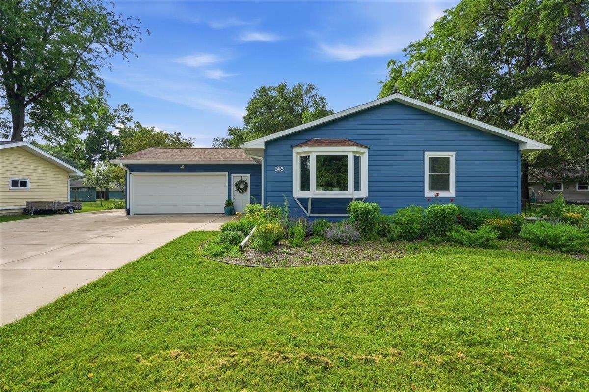 Blue single-story house with a two-car garage, white-trimmed bay window, and landscaped front lawn.