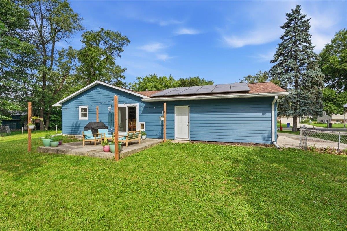 Blue home's rear exterior with rooftop solar panels, patio seating, and a broad green lawn.