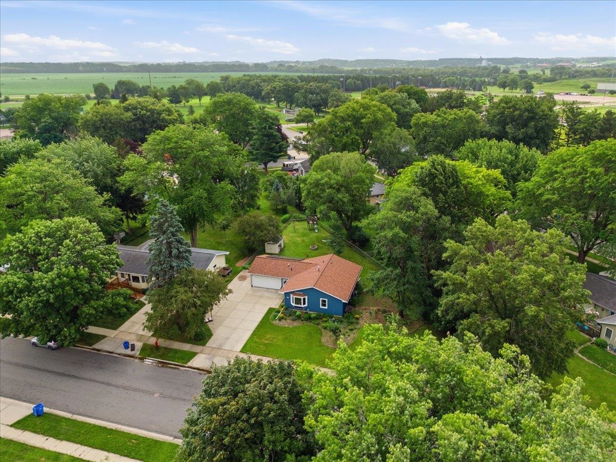 Blue house with a broad driveway and tree-filled yard, viewed from above.