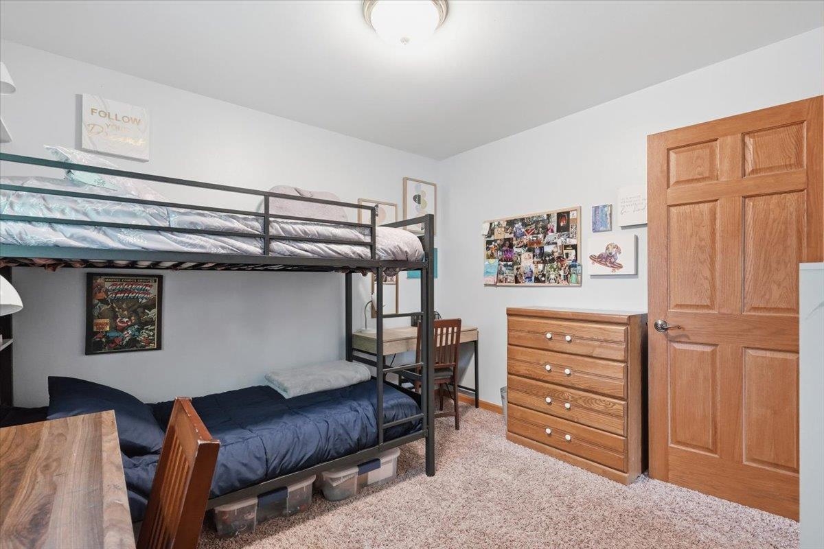 Bedroom with a black metal bunk bed, navy bedding, wooden dresser, and small desk.