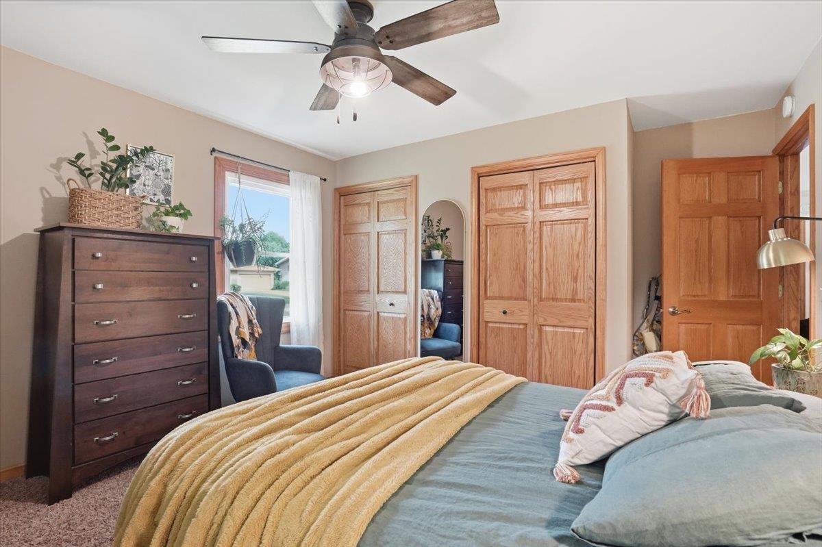 Bedroom with blue-green bedding, a mustard throw, wooden closet doors, and a ceiling fan.
