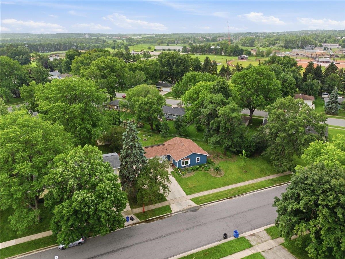 Blue single-story house with a reddish-brown roof, lawn, driveway, and mature trees.