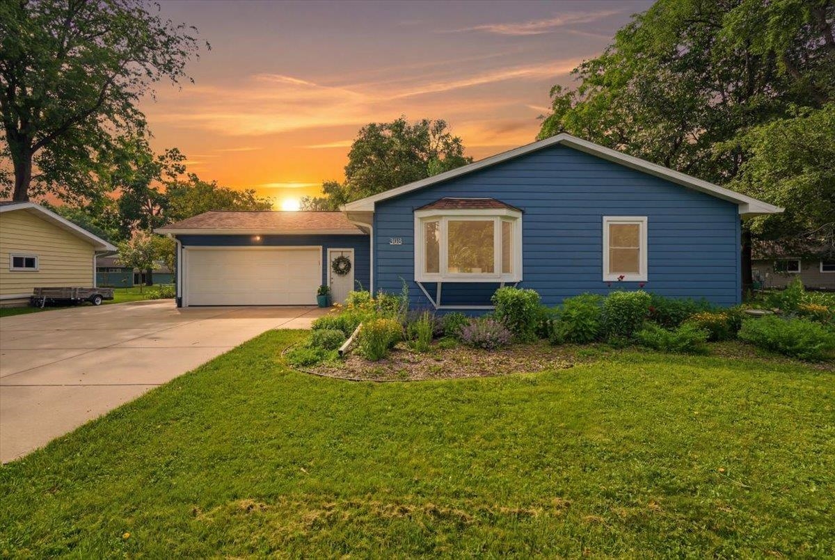 Blue single-story house with attached garage and bay window at sunset.