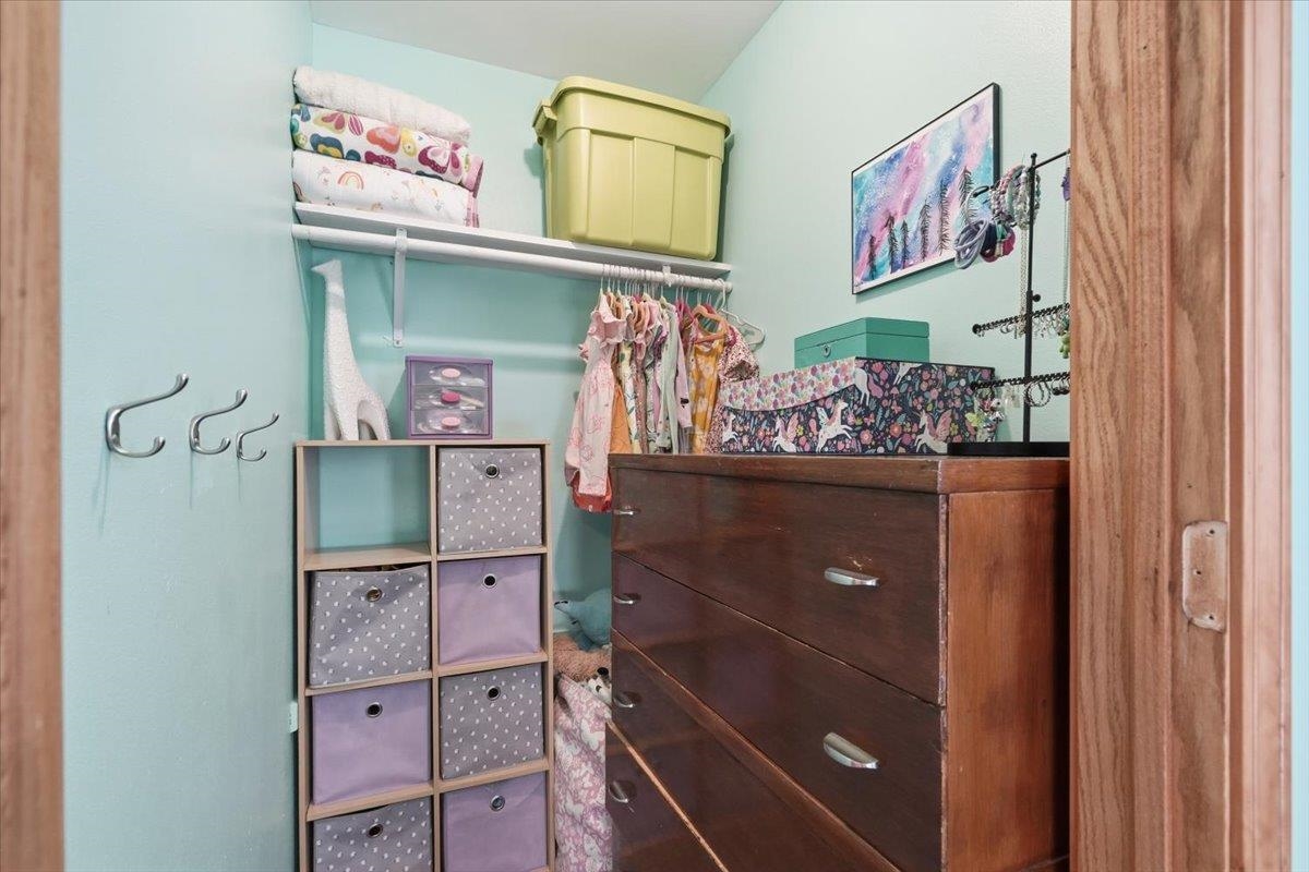 Walk-in closet with a dark wood dresser, cubby storage, and hanging clothes.