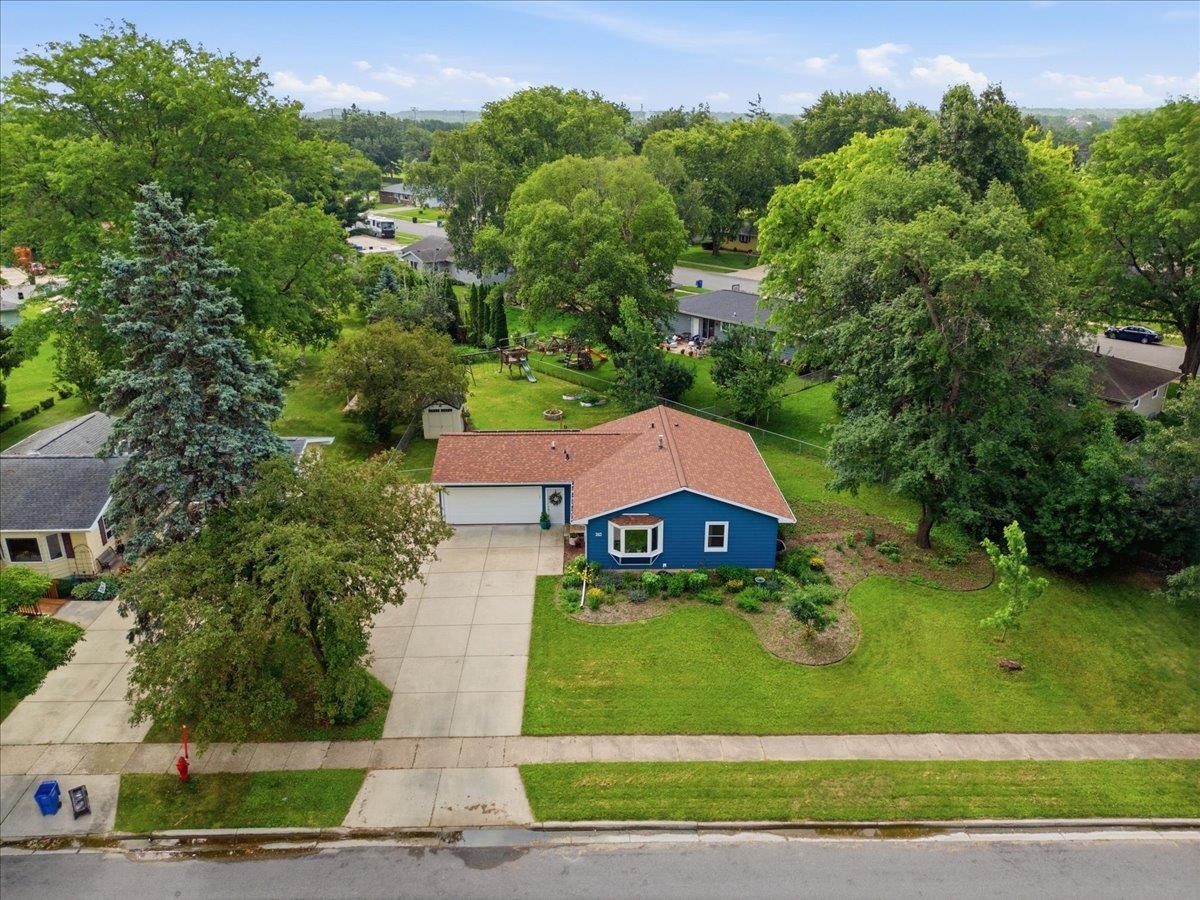 Blue single-story home with an attached garage, wide driveway, and tree-lined lawn.