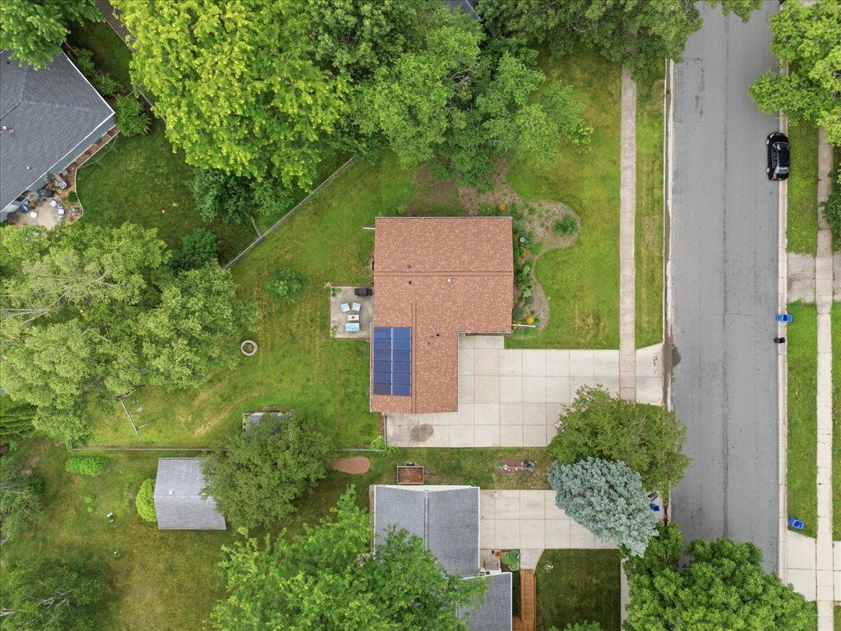 Aerial view of the home and tree-lined lot, with rooftop solar panels and a broad concrete driveway.