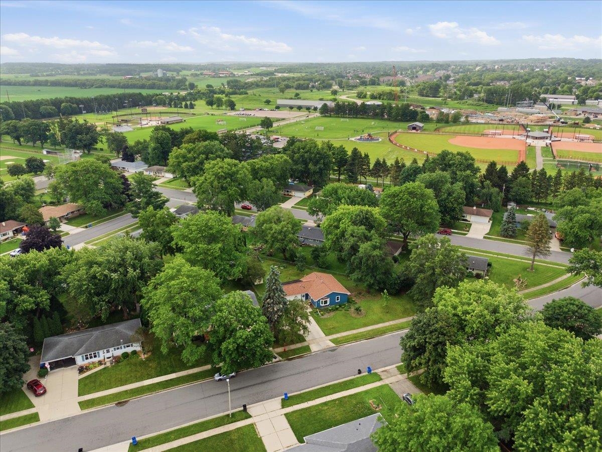 Aerial view of a blue house on a tree-lined street beside sports fields.