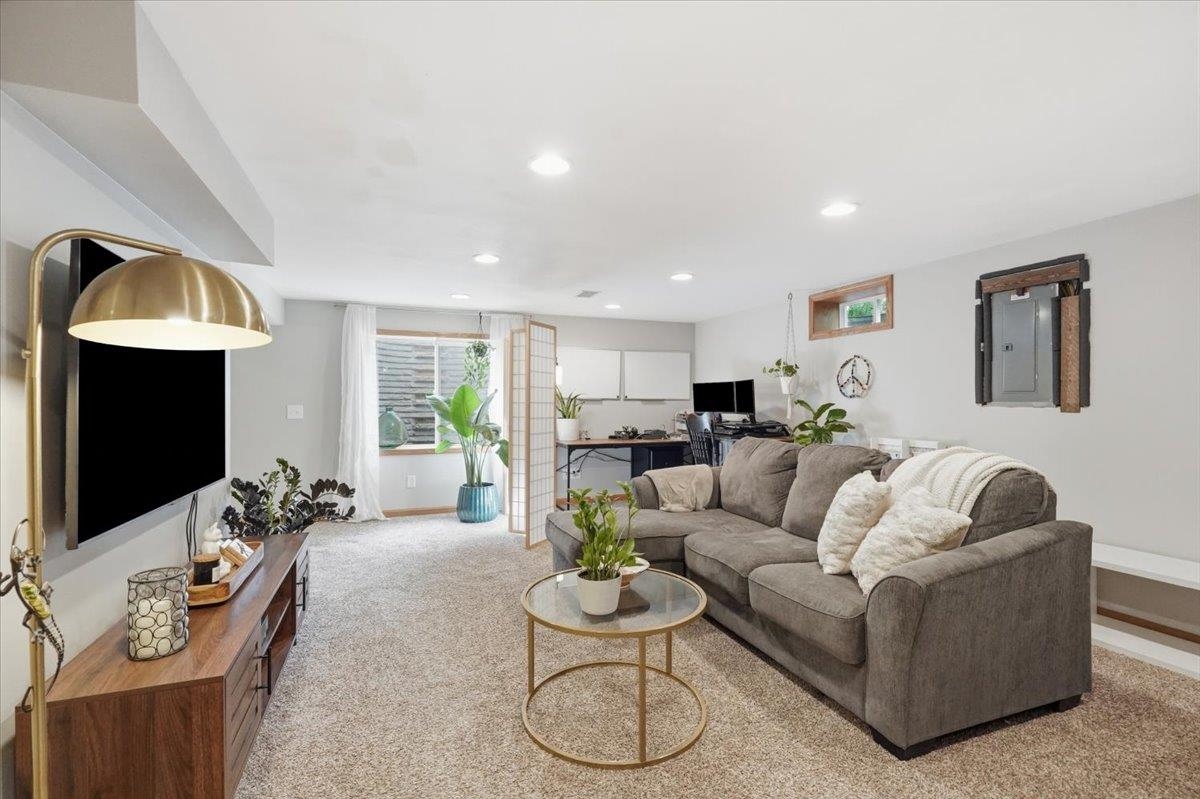 Furnished living room with gray sectional, wall-mounted television, and adjoining desk area.