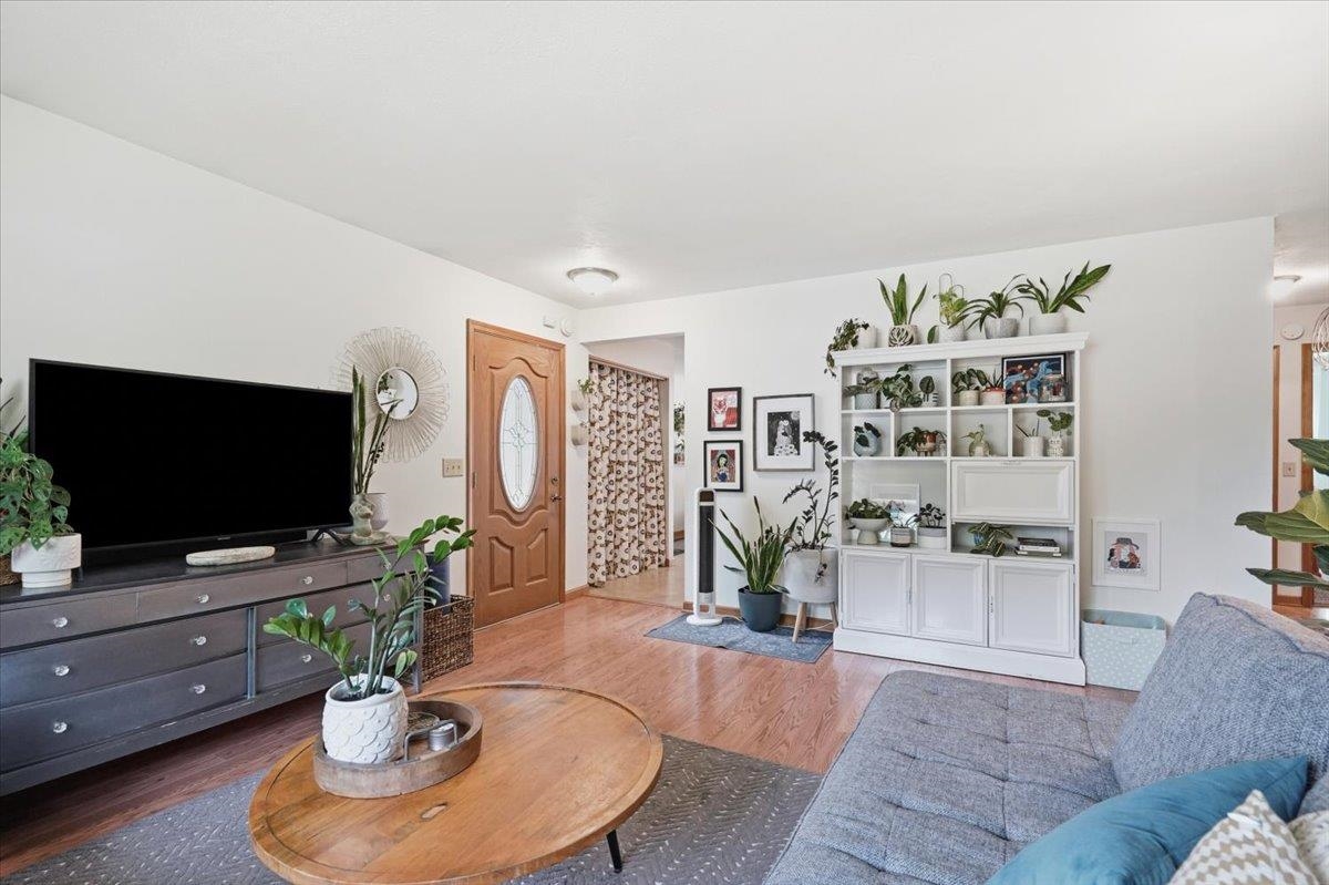 Living room with hardwood floors, gray sectional, oval coffee table, and plant-filled white shelving.