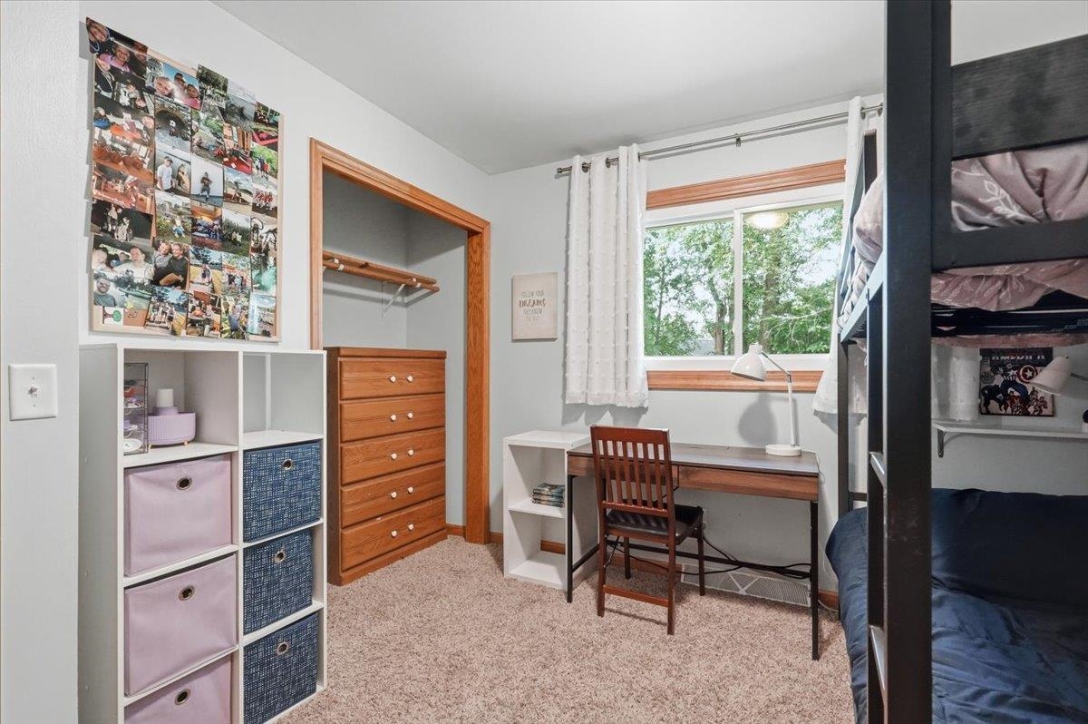 Bedroom with a black bunk bed, desk beneath a window, and wooden closet drawers.