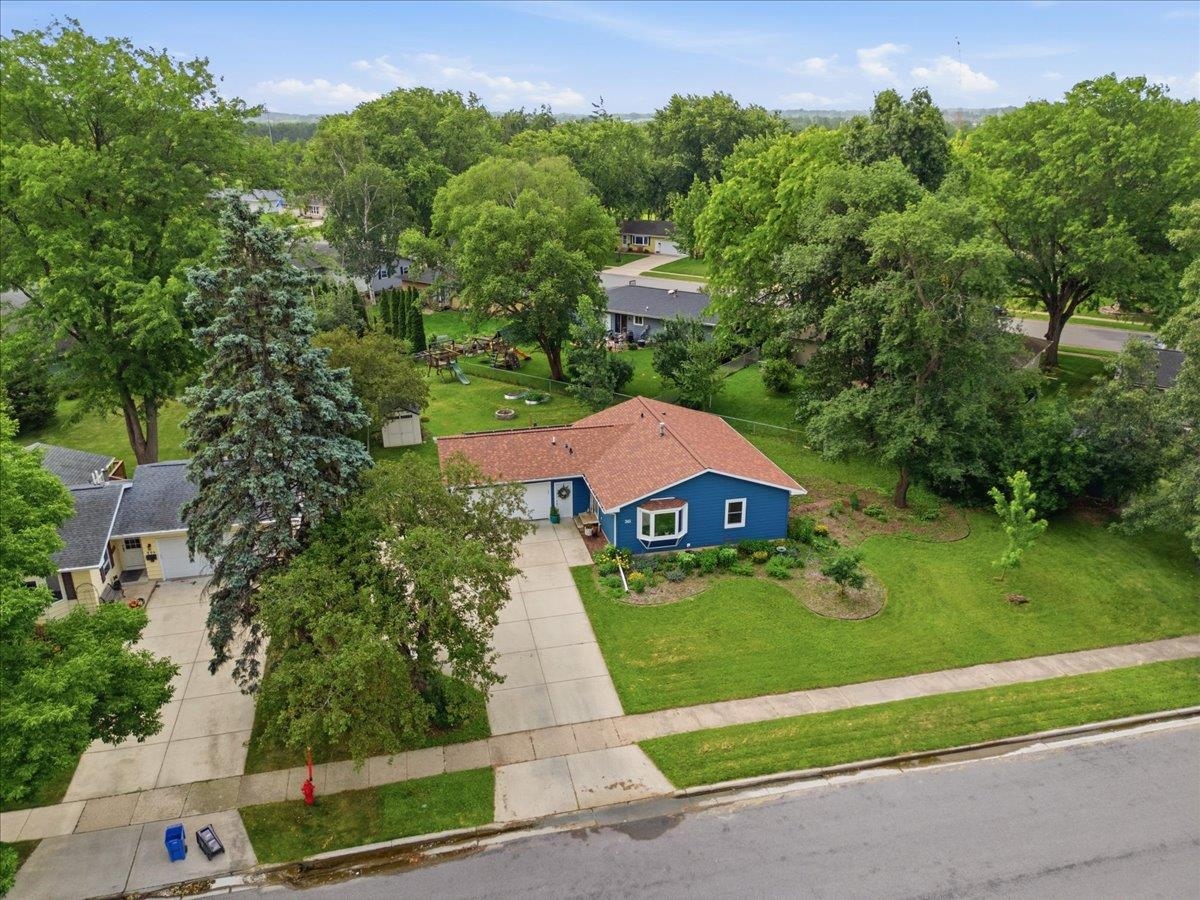 Blue single-story house with a reddish-brown roof, driveway, and broad tree-lined lawn.