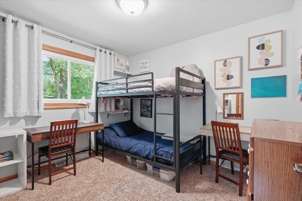 Bedroom with a black metal bunk bed between two desks and a large window overlooking trees.