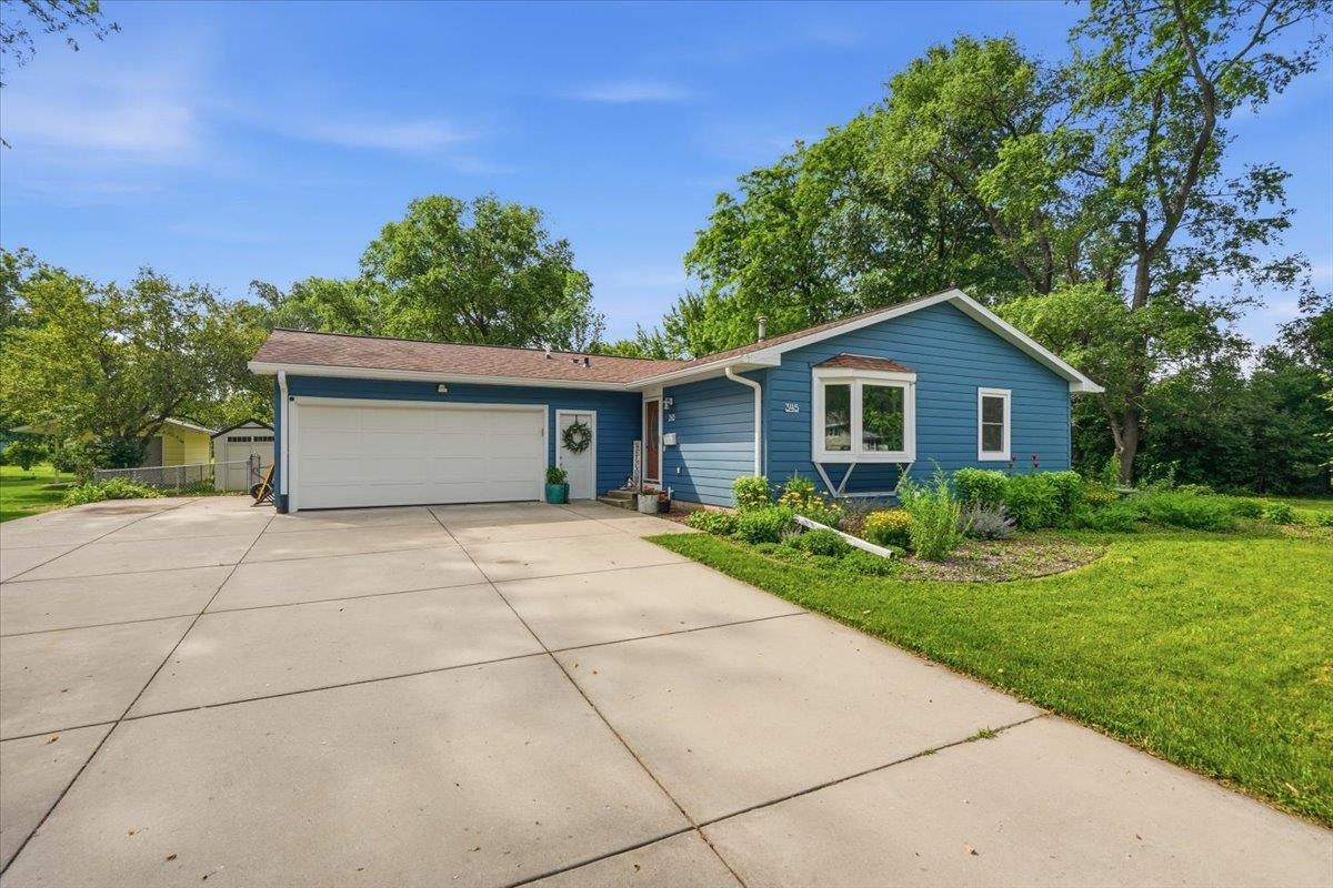 Blue single-story home with an attached two-car garage, broad concrete driveway, and landscaped front yard.