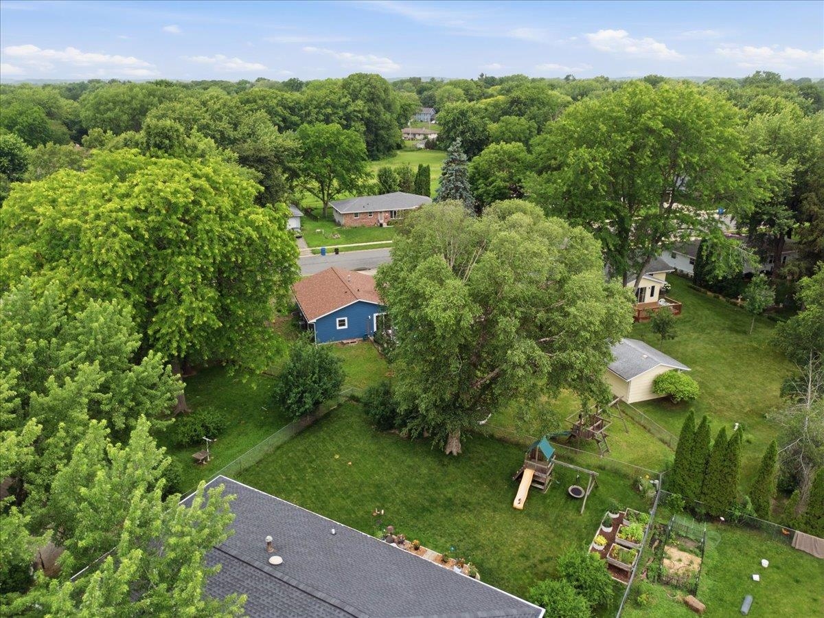 Aerial view of a residential backyard with mature trees, a playset, and garden beds.