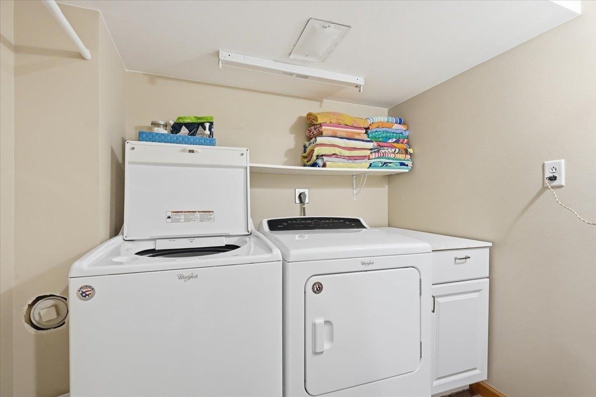 Laundry room with matching white washer and dryer beneath a shelf of folded towels.