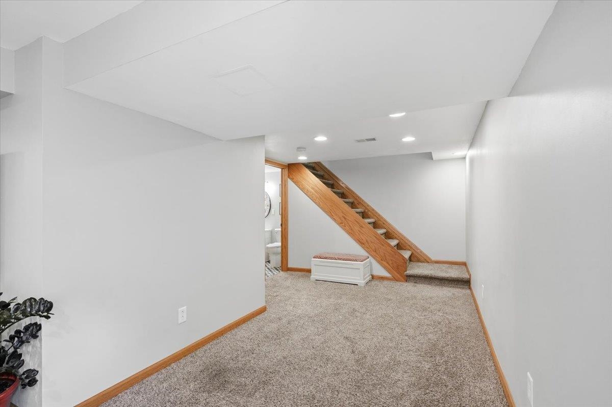 Finished basement with carpeted floor, wood staircase, and a small bench beneath the stairs.