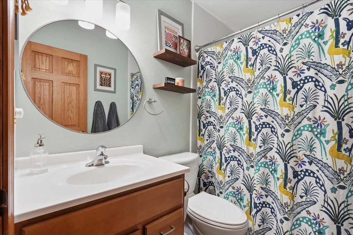 Bathroom with a wood vanity, round mirror, and colorful botanical-patterned shower curtain.
