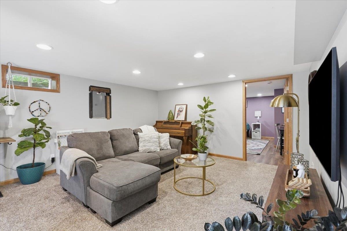 Living room with a gray sectional sofa, beige carpet, piano, and doorway to a purple room.