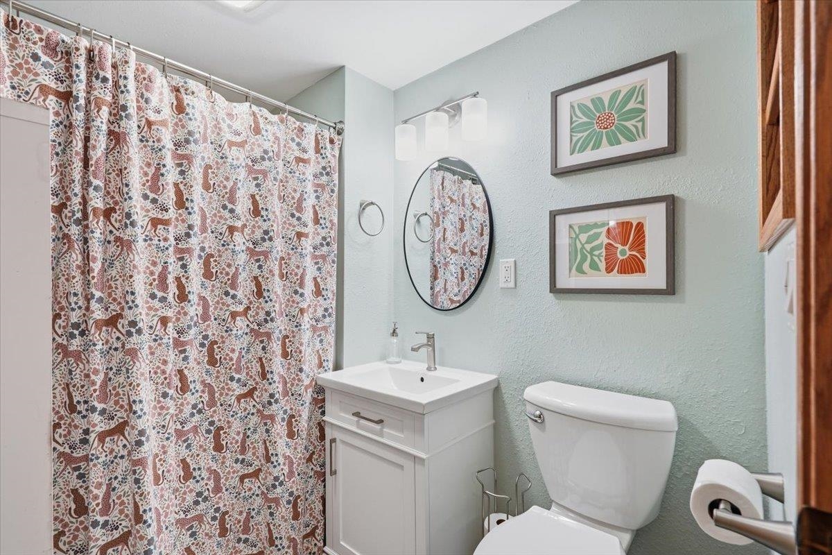 Bathroom with a white vanity, oval mirror, and patterned shower curtain.