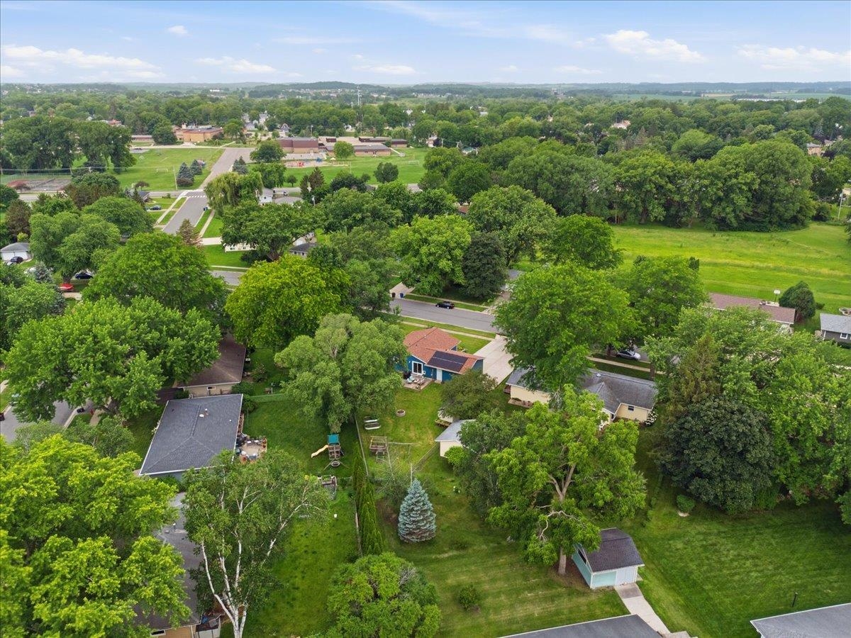 Aerial view of a tree-filled residential neighborhood with spacious yards and open fields nearby.