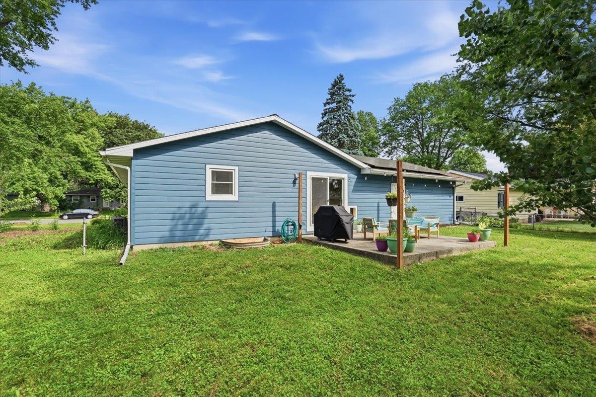 Blue single-story home with a concrete patio, outdoor seating, and potted plants.