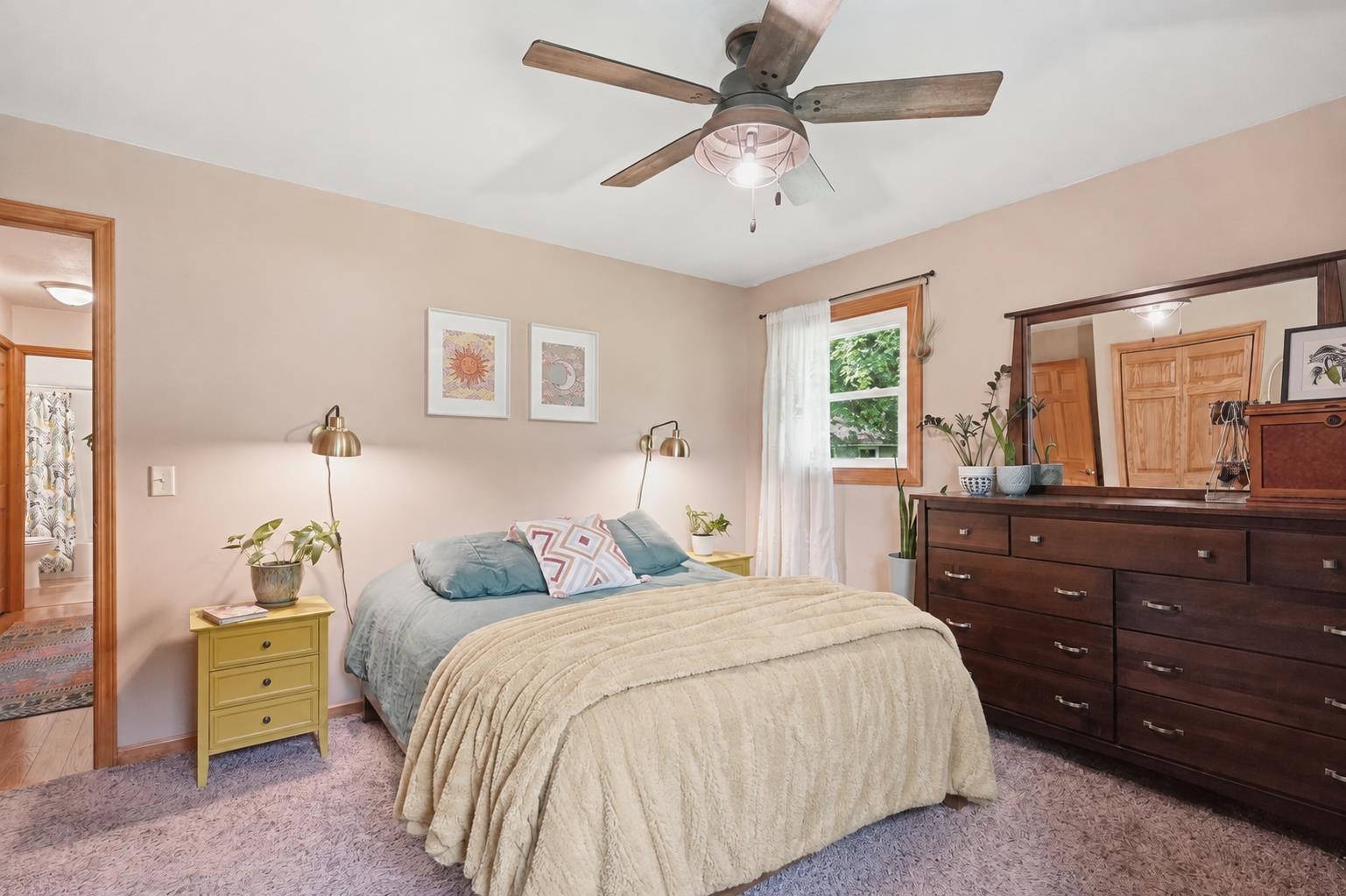 Bedroom with a cream-quilted bed, dark wood dresser and mirror, and ceiling fan.