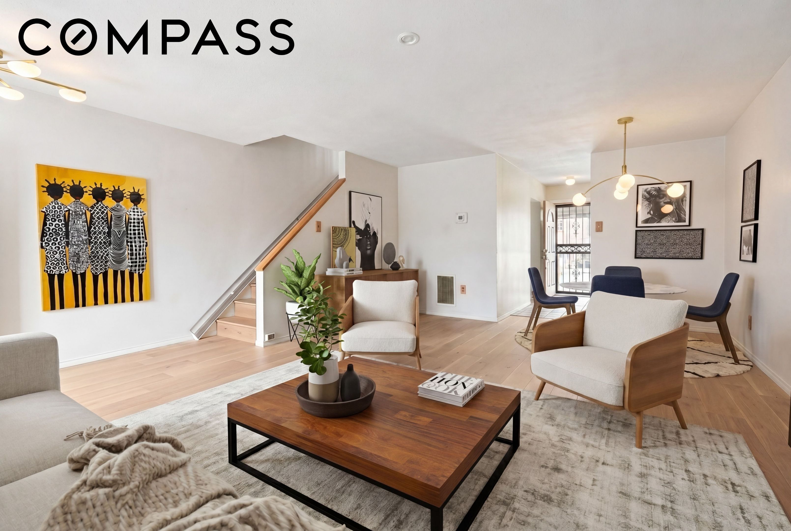 Staged living room with a staircase, cream chairs, wood coffee table, and bold yellow wall art.