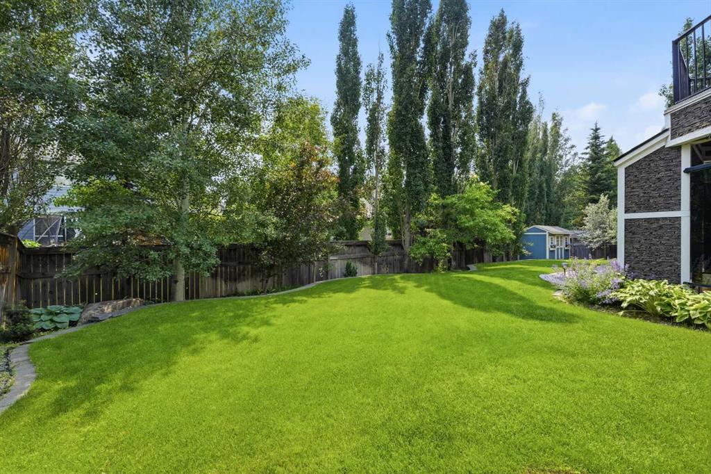 Backyard with a broad lawn, mature trees, flower beds, and a small blue shed.