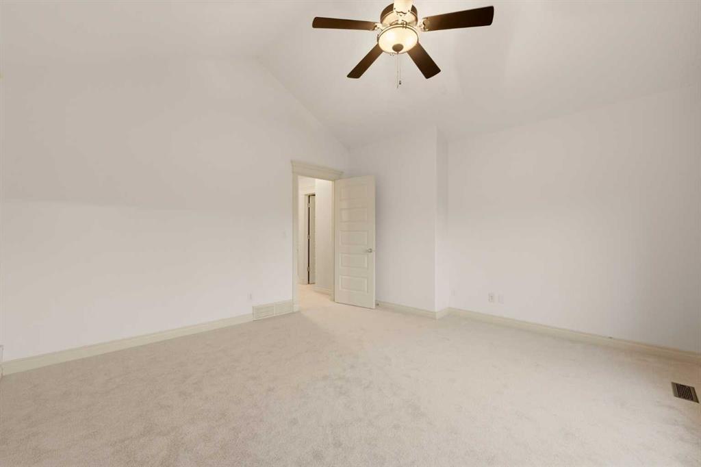 Empty carpeted bedroom with a ceiling fan and an open doorway.