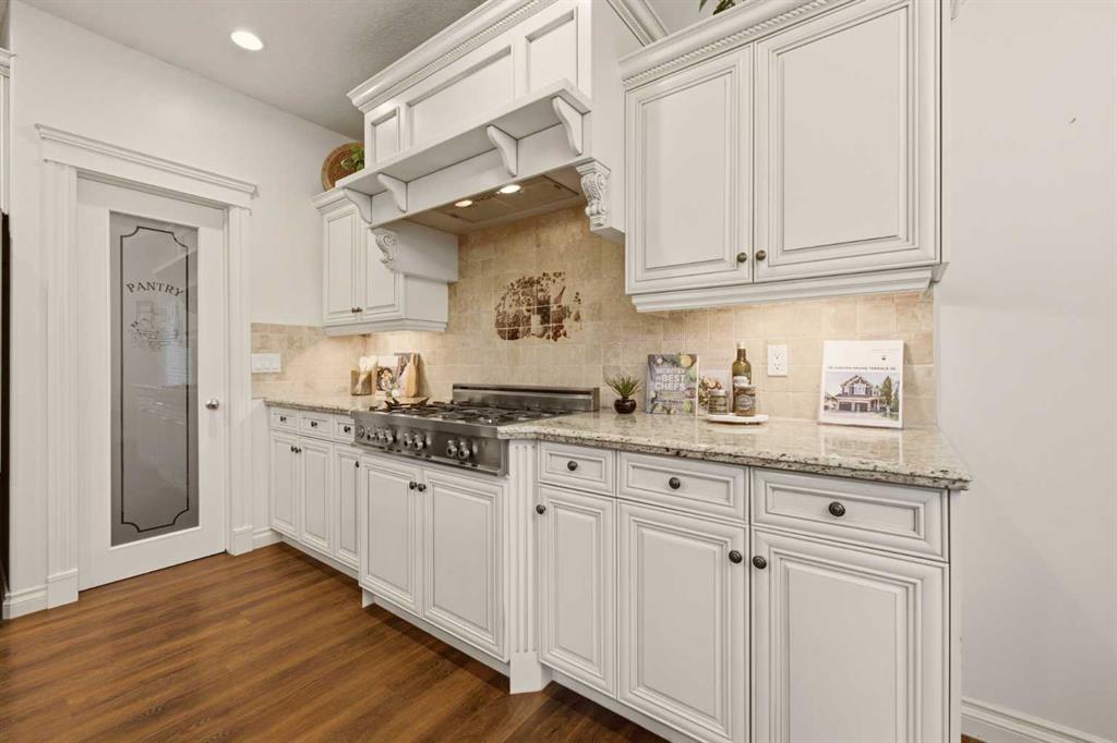 Kitchen with white cabinetry, a decorative range hood, stainless gas range, and glass-panel pantry door.