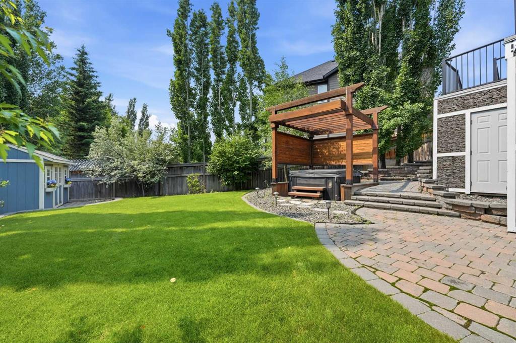 Backyard with a broad lawn, mature trees, and a wood pergola beside a curved brick-paver walkway.