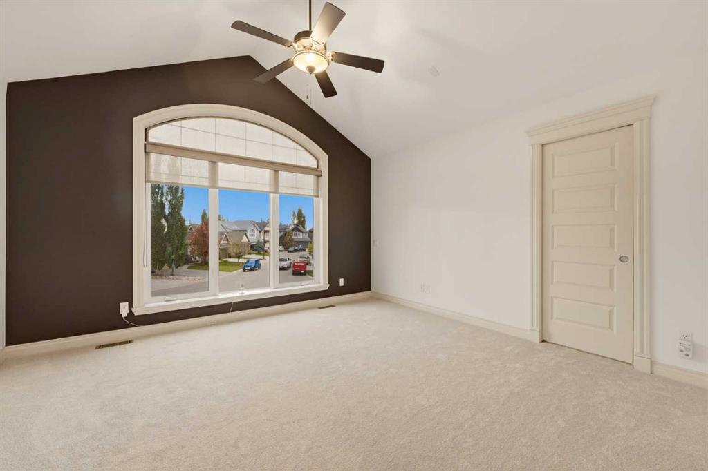 Empty bedroom with an arched street-facing window, dark accent wall, and ceiling fan.