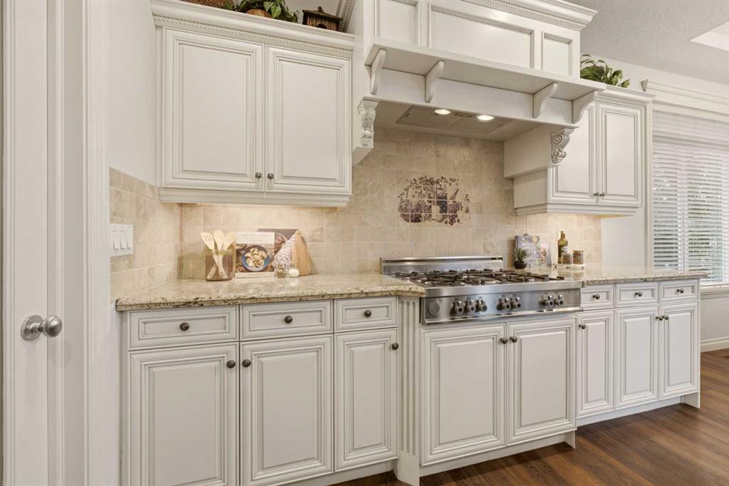 Kitchen with white cabinetry, a large stainless steel gas range, and warm wood flooring.