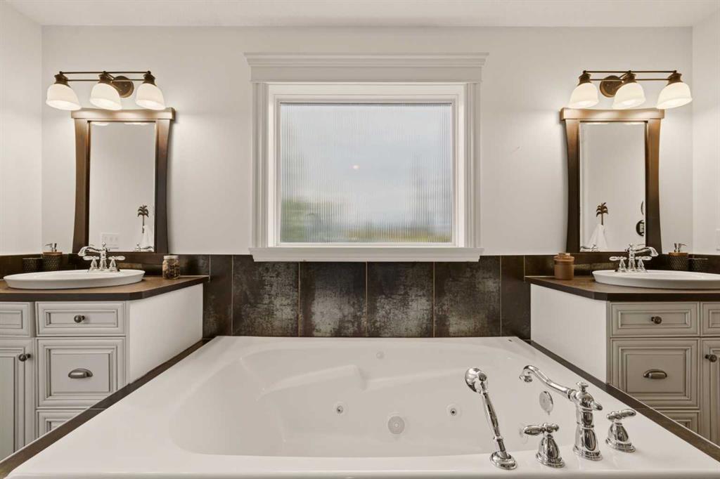 Bathroom with a large jetted tub, dark tile surround, and matching vanities.