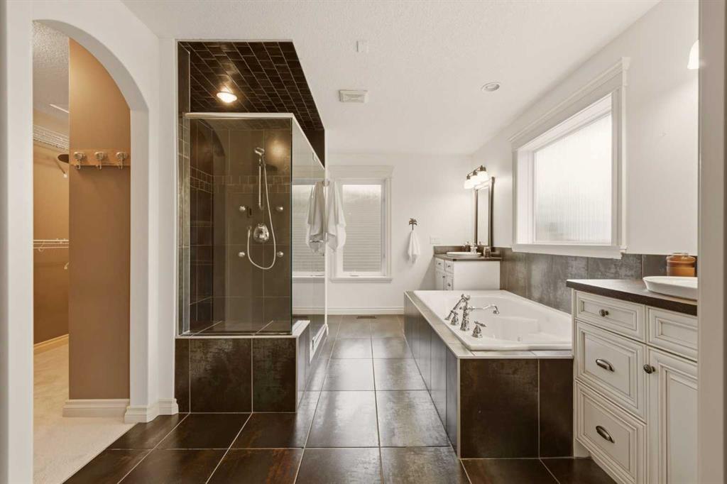 Bathroom with a dark tiled glass shower, soaking tub, white vanity, and arched opening to a walk-in closet.