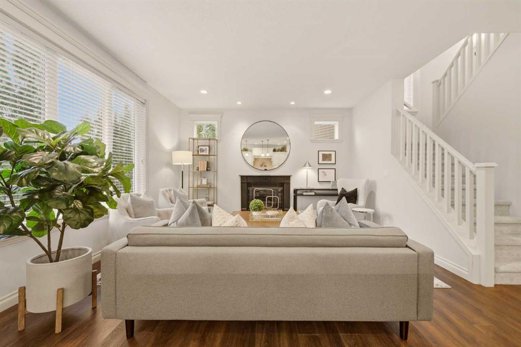 Staged living room with a fireplace, round mirror, large windows, and staircase.