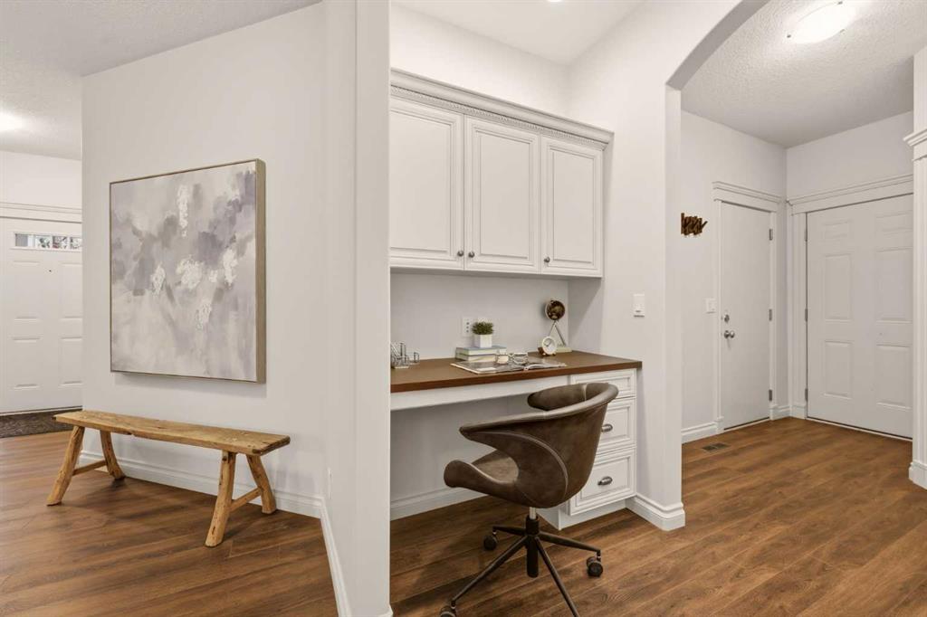 Home office nook with white built-in desk, brown swivel chair, and wooden bench beneath abstract art.