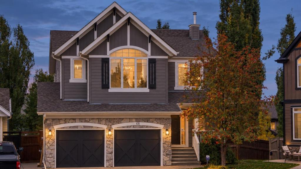 Two-story gray home with a stone double garage and warm window lights at dusk.