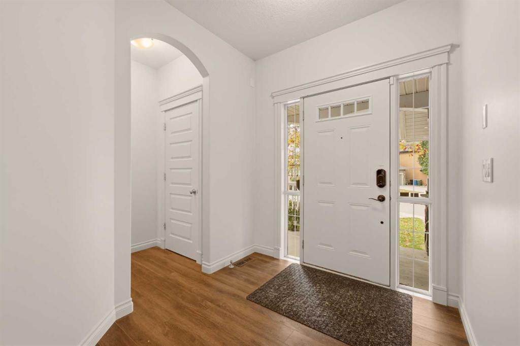 Entry foyer with a white front door and sidelights, arched hallway opening, and hardwood floors.