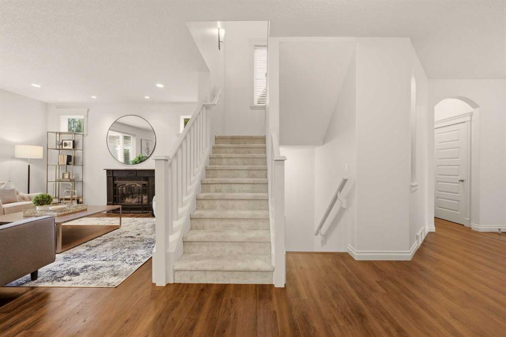 Carpeted staircase with white railings beside a furnished living room and fireplace.