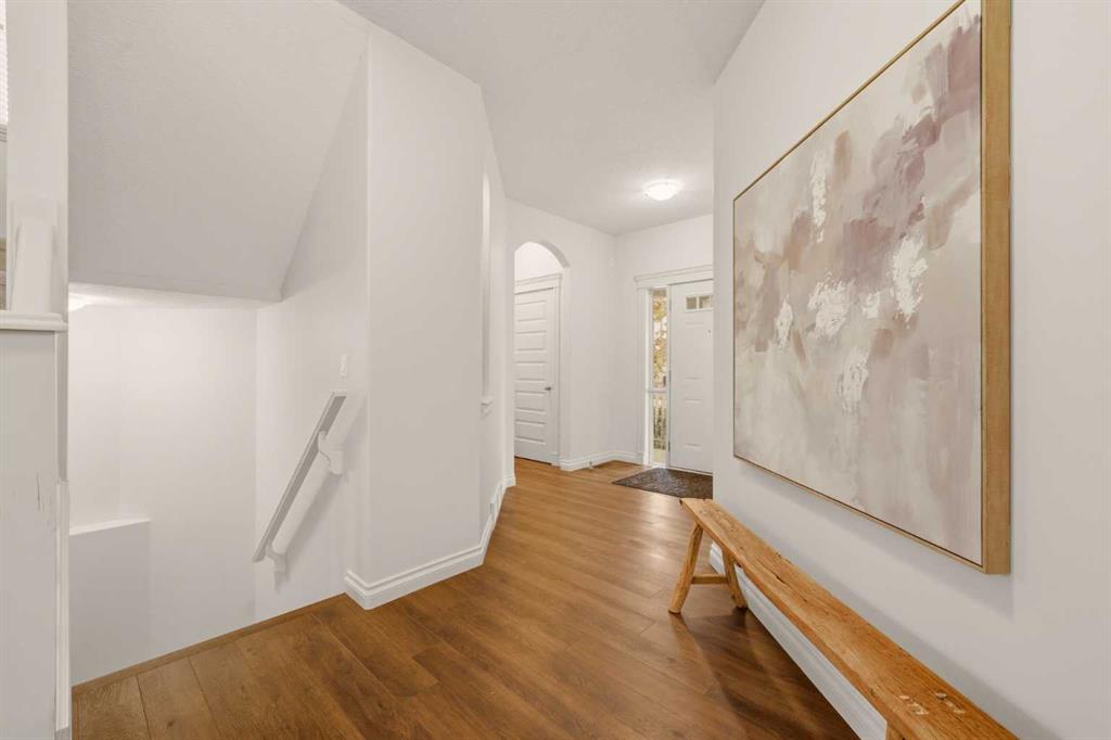 Entry hallway with warm wood floors, a staircase, framed abstract artwork, and a wooden bench.