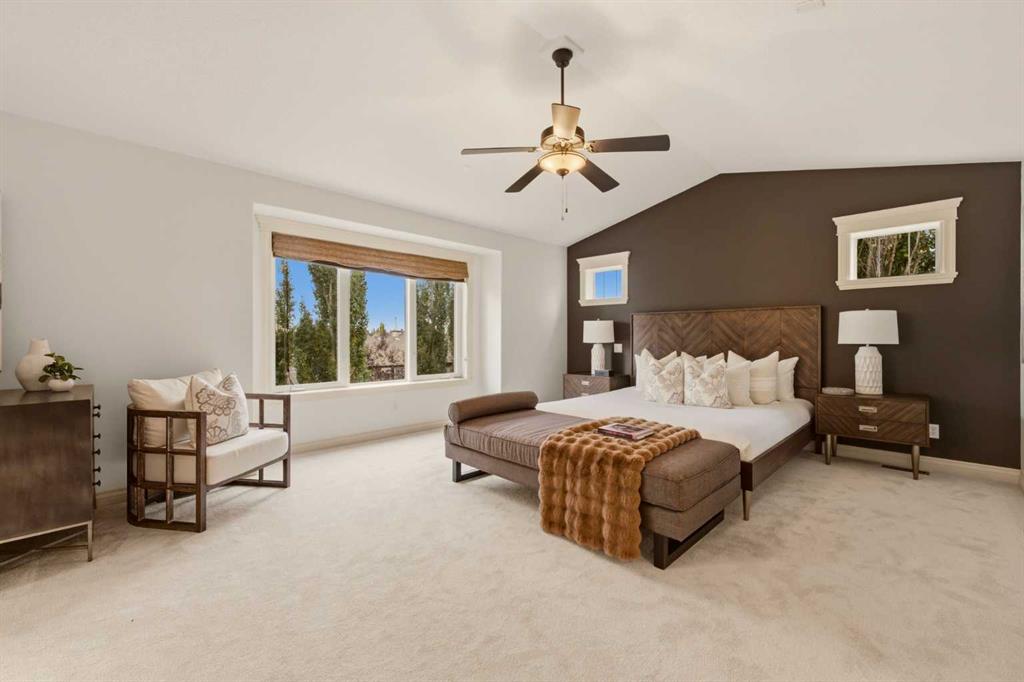 Staged bedroom with an upholstered bed, cushioned chair, and large window.