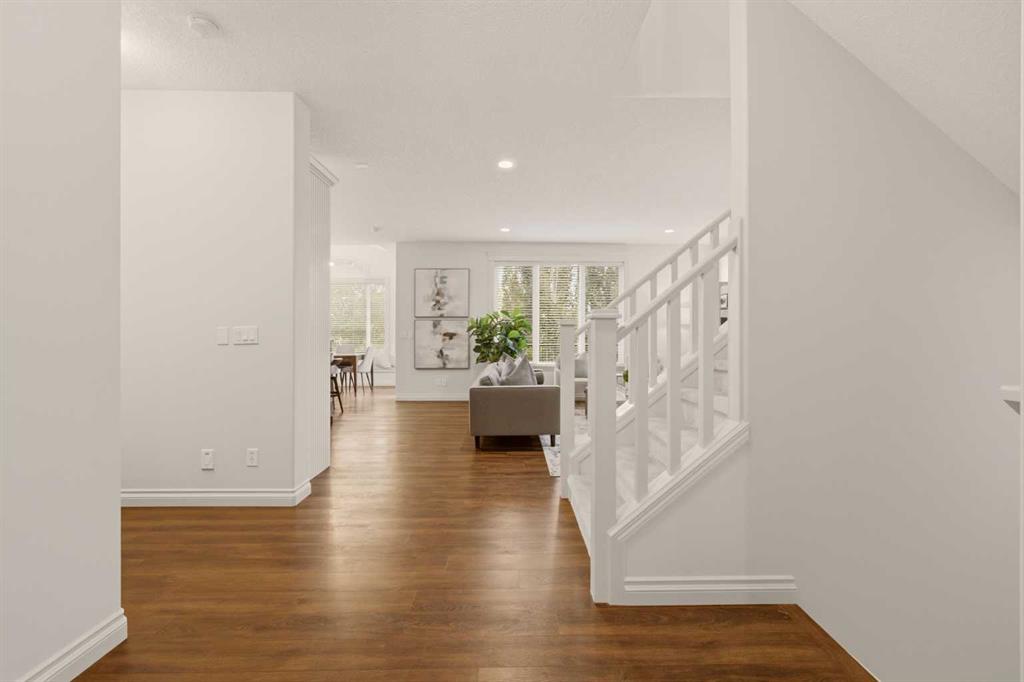 Entry hall with warm wood floors, a white staircase, and a living area beyond.