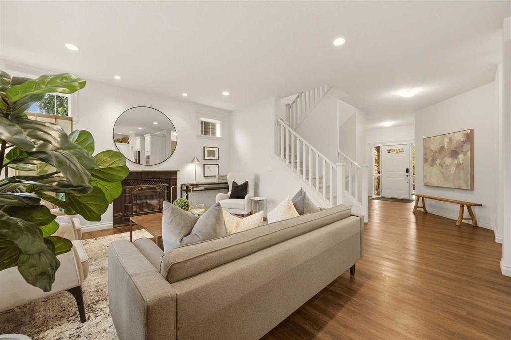 Staged living room with a fireplace, leafy plant, and staircase beside the front entry.