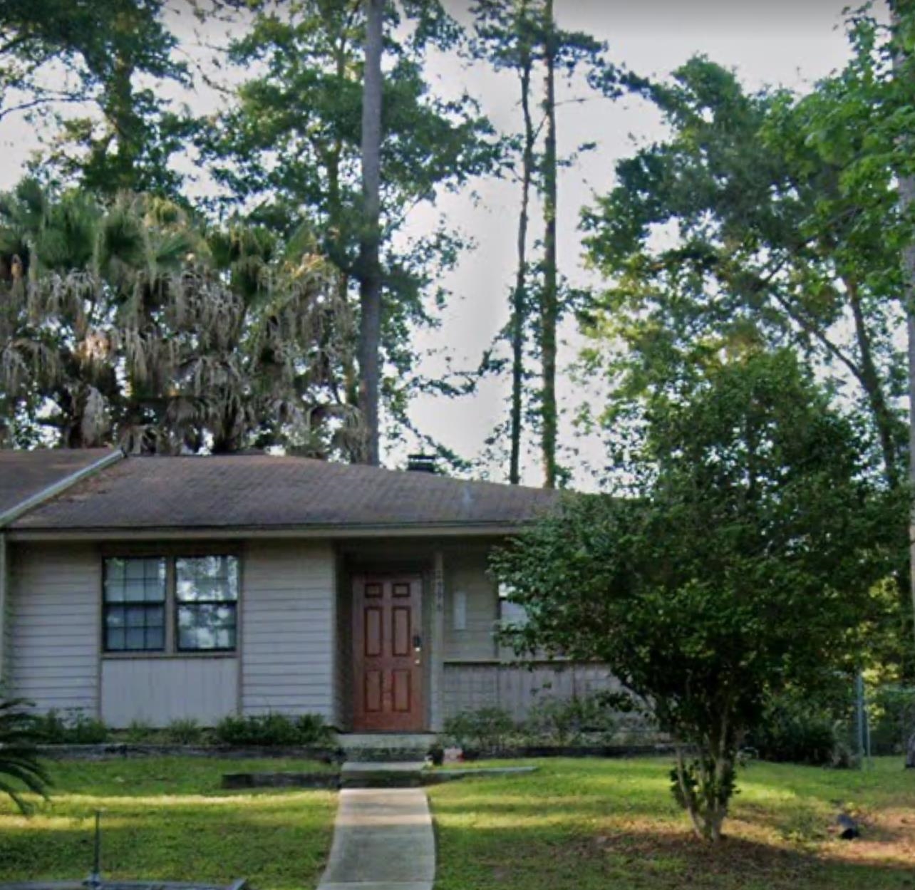 Single-story house with a brown front door, concrete walkway, and mature trees.