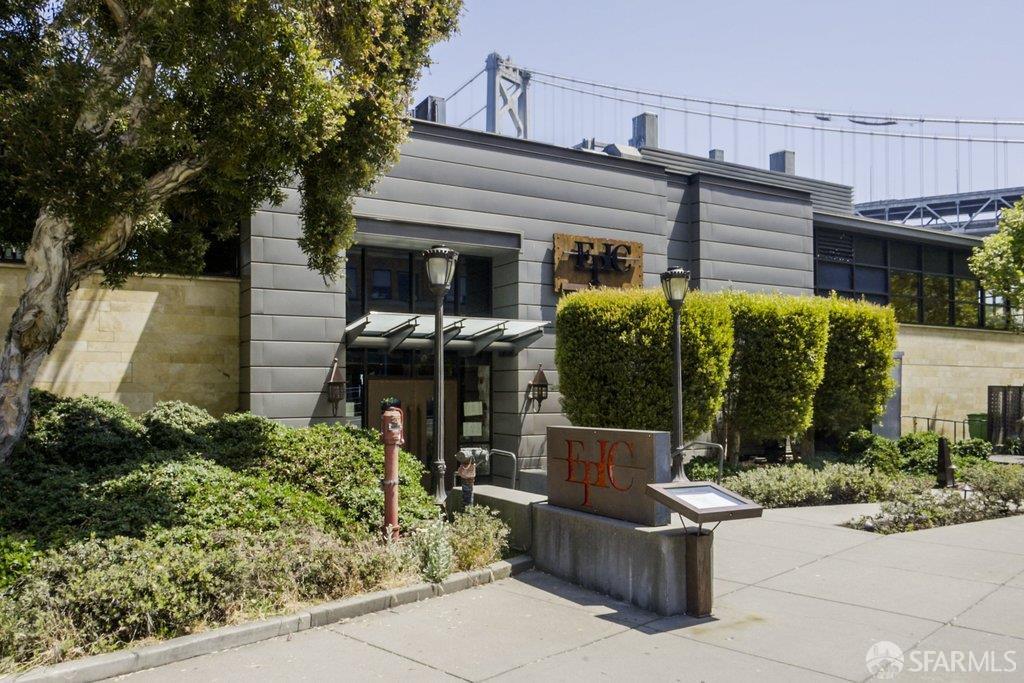 Modern residential building entrance with landscaped shrubs and the Bay Bridge behind it.