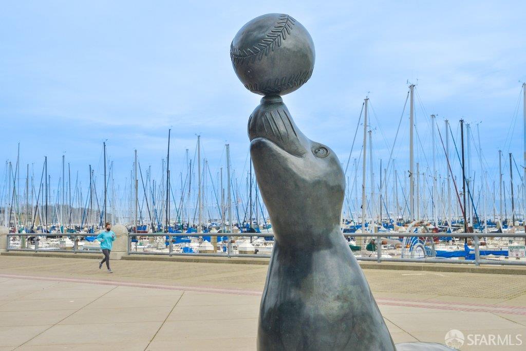 Sea lion sculpture balancing a baseball beside a marina filled with sailboats.