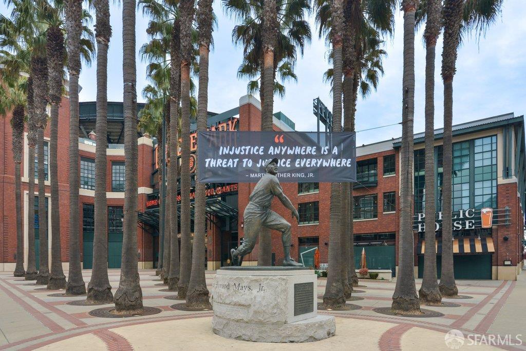 A baseball player statue in a palm-lined plaza outside a red-brick ballpark.