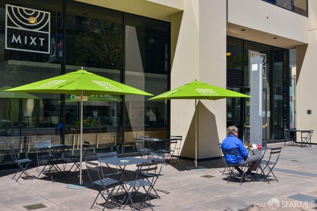 Street-level storefront with green umbrellas shading outdoor café tables and chairs.